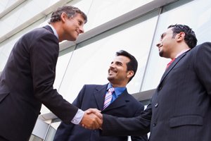 Two men in suits shaking hands; a third man smiles.