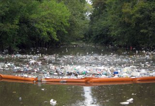 Floating orange inflatable plastic boom holding back most floating trash on a river