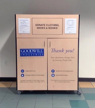 Large wheeled rectangular bin with a push in section at the labeled “Donate Clothing, Shoes, and Books” surrounded by more detailed instructions for dropping off donations. The bin has doors with handles on the front that can be unlocked for easy unloading.