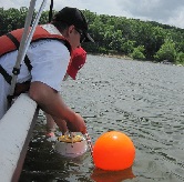 A researcher in a boat collects an instrument from the water of a reservoir.