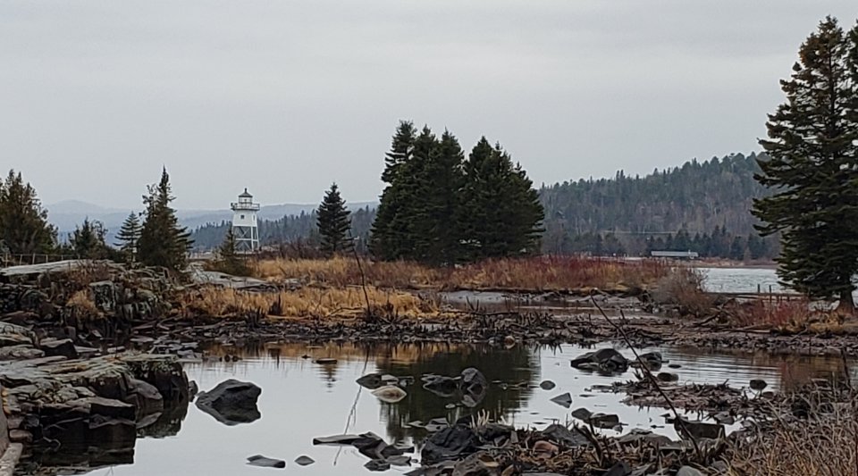 Rocky shore of Lake Superior with a lighthouse at the entry to a harbor.