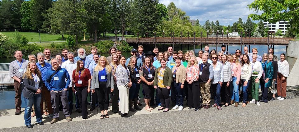 Group photo of attendees with Spokane River and walking bridge in background.