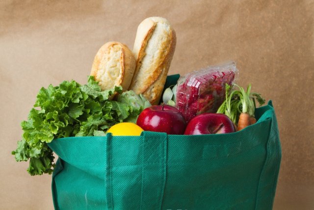 This is a green, reusable bag of groceries including a baguette, lettuce, carrots, radishes and lemons