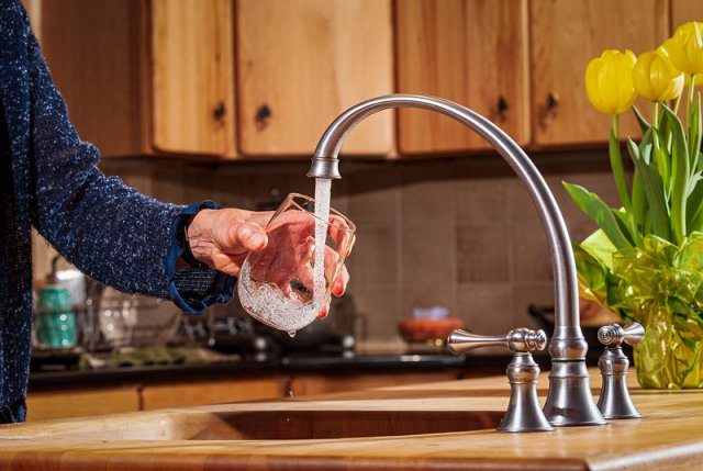 A hand filling a glass with water from a kitchen sink faucet