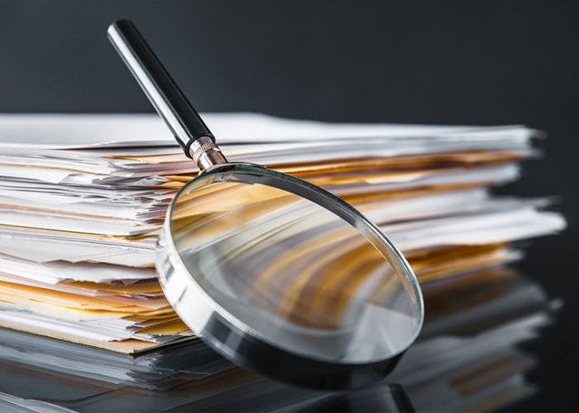 A stack of folders full of documents with a magnifying glass leaning up against the stack.