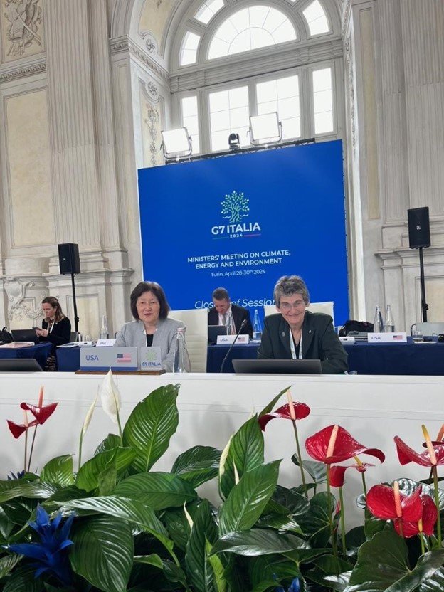OITA Assistant Administrator Nishida with EPA Deputy Administrator McCabe sitting in at table and smiling at camera in front of G7 Italia 2024 sign