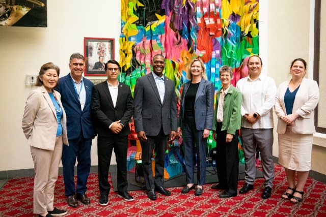 Eight CEC Council Members standing in front of colorful artwork smiling at camera.
