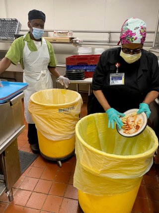 Image of two people scraping food off a plate in a kitchen. 