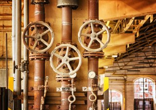 three metal pipes and wheel valves are seen running down the wall of an industrial facility