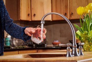 Person fills a glass of water under a kitchen faucet