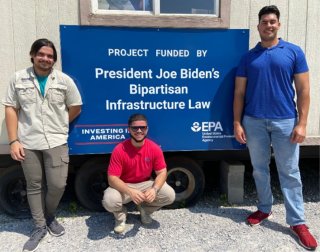 Student volunteers standing in front of a sign for the Bipartisan Infrastructure Law