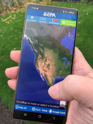 A person's hand holding a mobile device with the CyAN app running and showing a map of North America.