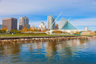 View of Milwaukee skyline with water in foreground and blue and cloudy sky in the background. 