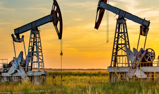 Two pumpjacks for oil extraction in the foreground of an open field, deep yellow sunset in the background. 